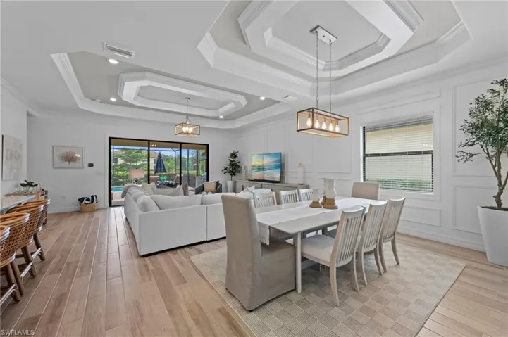 Dining space featuring a raised ceiling, light wood finished floors, and crown molding