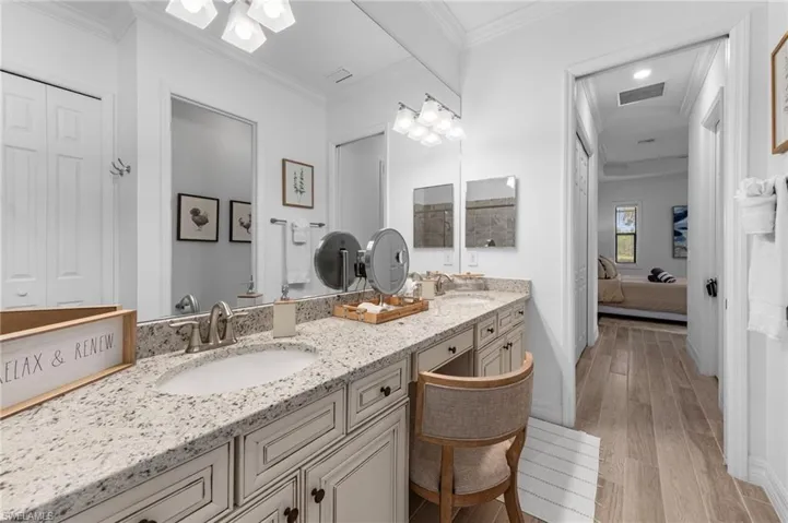 Ensuite bathroom featuring light wood-type flooring, double vanity, ornamental molding, and a closet