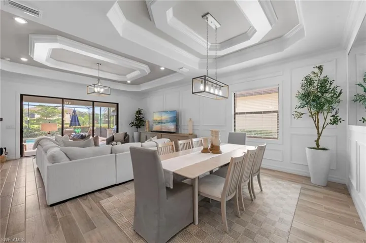 Dining area with a raised ceiling, a chandelier, light wood finished floors, crown molding, and a decorative wall
