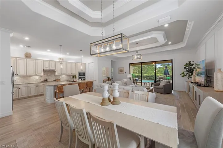 Dining area with a raised ceiling, light wood finished floors, ornamental molding, and recessed lighting