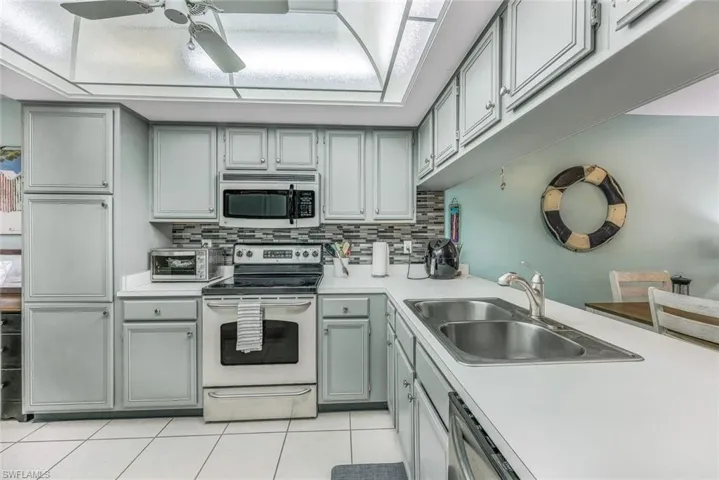 Kitchen with stainless steel appliances, backsplash, sink, ceiling fan, and light tile floors