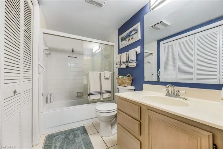 Full bathroom with tile flooring, bath / shower combo with glass door, vanity, and toilet