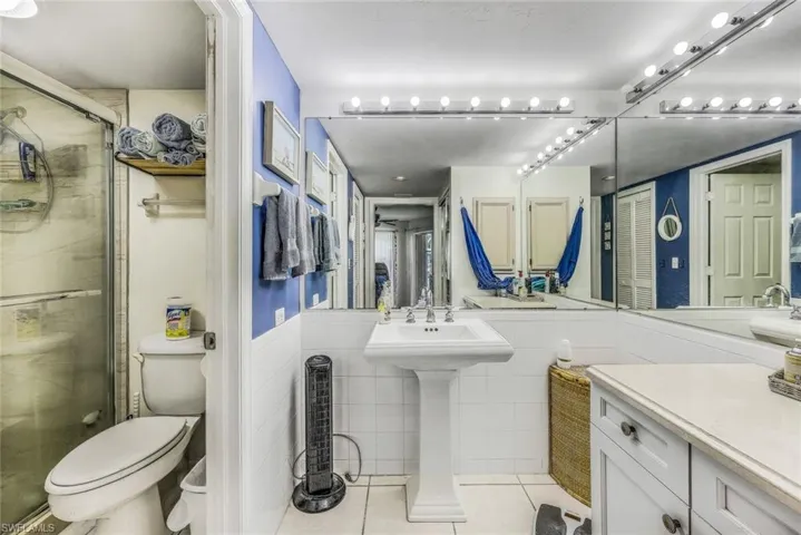 Bathroom featuring walk in shower, tile flooring, tile walls, sink, and toilet