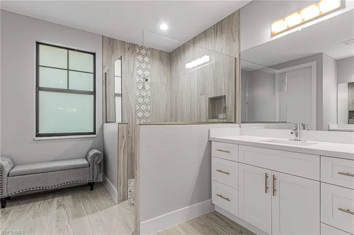Full bathroom with vanity, a walk in shower, light wood-type flooring, and a textured wall