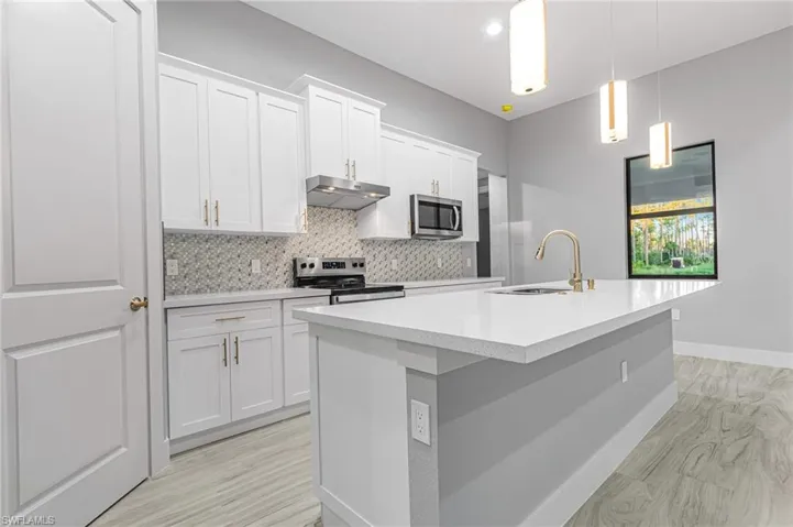 Kitchen featuring a center island with sink, stainless steel appliances, light wood-type flooring, and decorative light fixtures