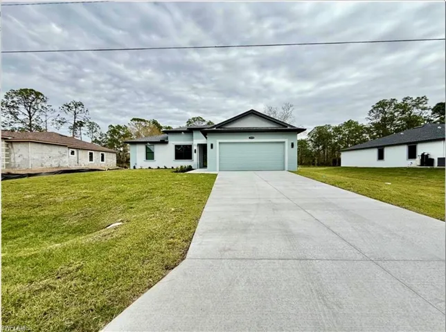 View of front of property with an attached garage, a front lawn, driveway, and stucco siding