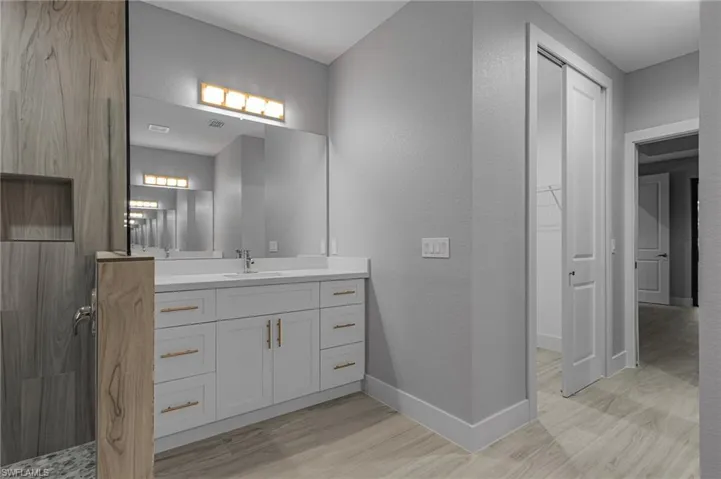 Bathroom featuring a textured wall, vanity, light wood-style flooring, and a walk in closet