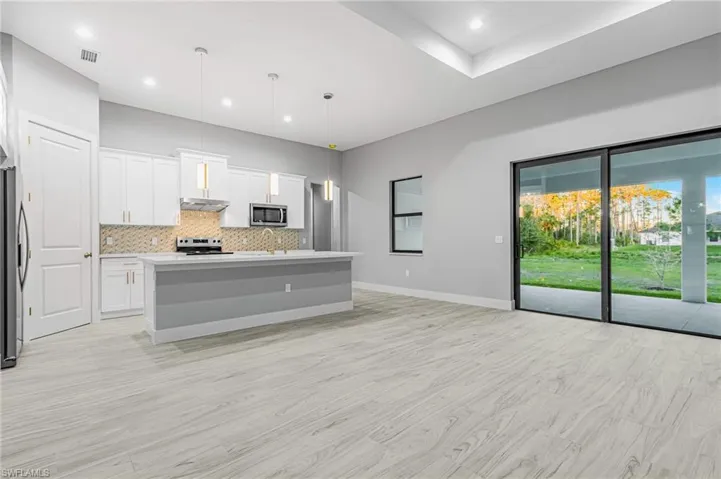Kitchen with white cabinetry, a center island with sink, decorative light fixtures, light wood-type flooring, and stainless steel appliances