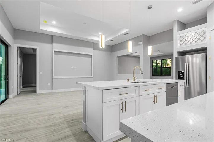 Kitchen featuring stainless steel appliances, light stone countertops, white cabinetry, decorative light fixtures, and light wood-style flooring