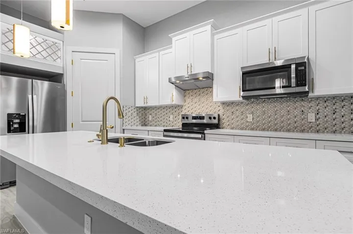 Kitchen with white cabinetry, stainless steel appliances, light stone counters, decorative light fixtures, and decorative backsplash