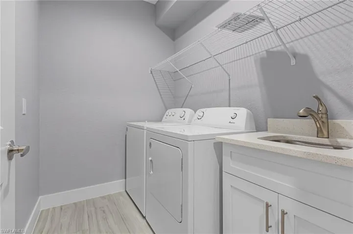 Laundry area featuring a textured wall, washer and dryer, light wood finished floors, and cabinet space