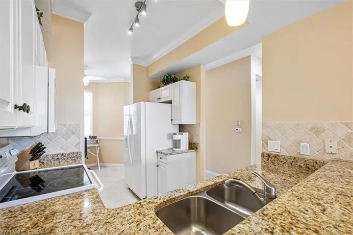 Kitchen with white cabinets, decorative backsplash, ornamental molding, white appliances, and light stone counters