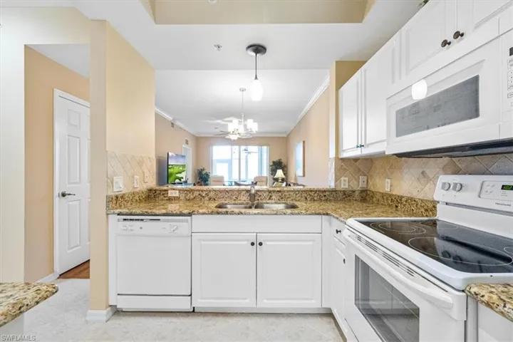 Kitchen with white appliances, backsplash, white cabinetry, light stone countertops, and decorative light fixtures