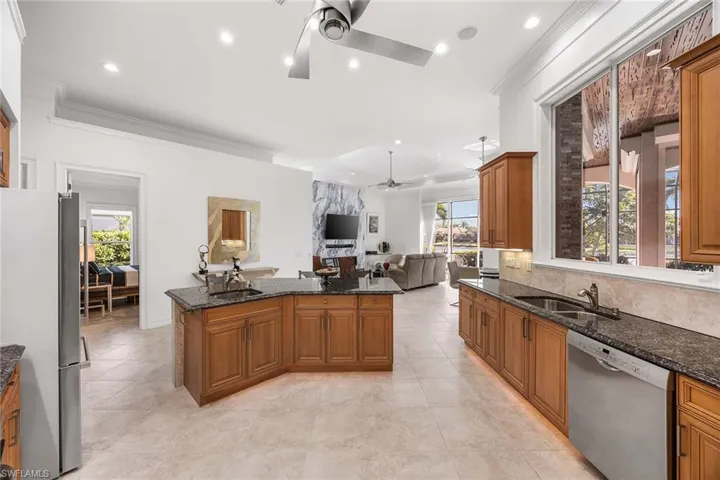Kitchen featuring brown cabinets, dark stone counters, stainless steel appliances, crown molding, and open floor plan