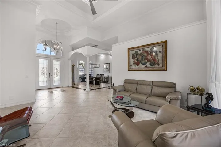 Tiled living area with arched walkways, french doors, a towering ceiling, a chandelier, and a desk