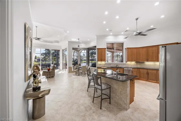 Kitchen with ceiling fan, brown cabinetry, appliances with stainless steel finishes, dark stone countertops, and a breakfast bar area