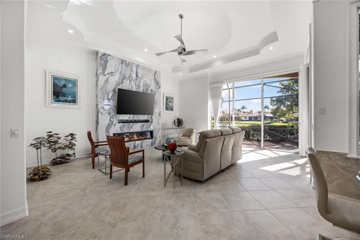 Living room with a fireplace, crown molding, a ceiling fan, light tile patterned floors, and recessed lighting