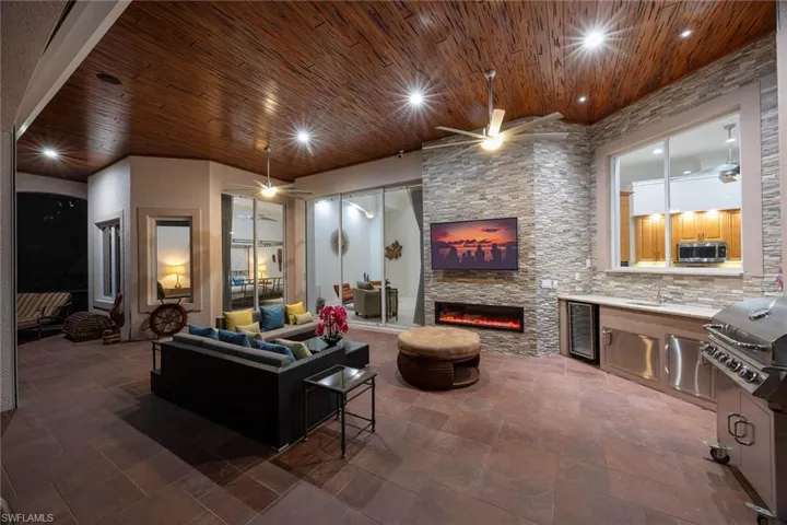 Living area with a stone fireplace, beverage cooler, a ceiling fan, dark stone finish flooring, and wooden ceiling