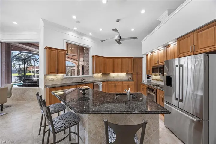 Kitchen with brown cabinets, dark stone countertops, stainless steel appliances, a center island with sink, and crown molding