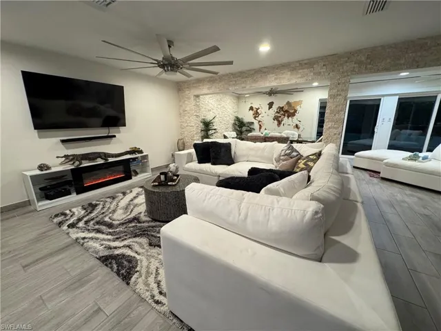 Living area featuring light wood finished floors, a glass covered fireplace, and ceiling fan
