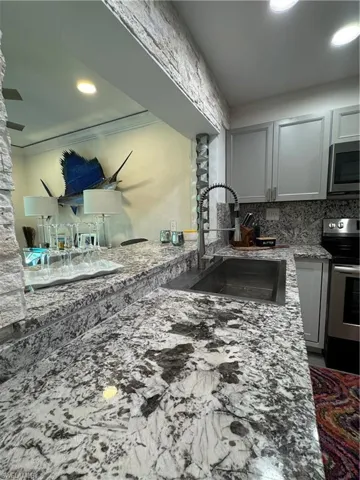 Kitchen featuring light stone countertops, range, recessed lighting, gray cabinets, and ornamental molding