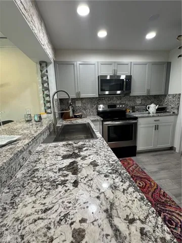 Kitchen featuring electric range, gray cabinets, backsplash, light stone counters, and recessed lighting