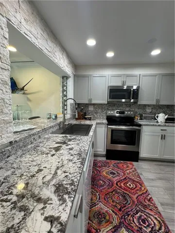 Kitchen featuring stainless steel appliances, light stone counters, tasteful backsplash, gray cabinets, and recessed lighting