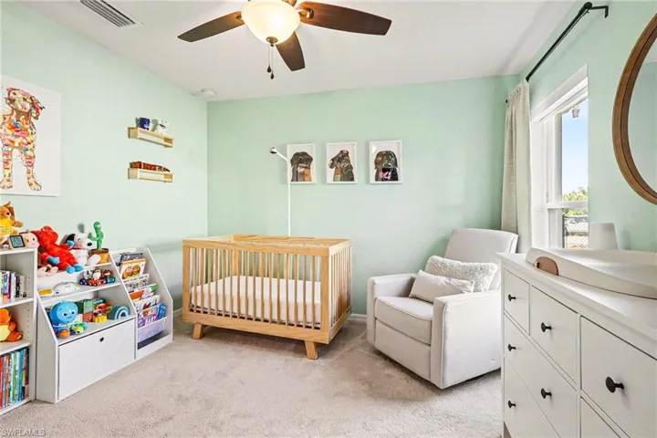 Bedroom featuring a crib, light colored carpet, and ceiling fan
