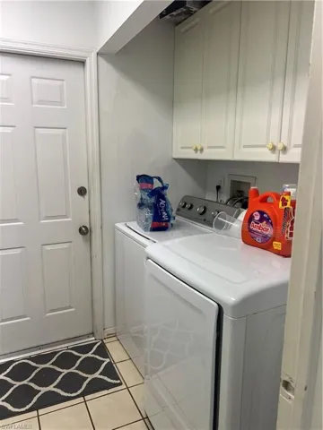 Laundry area with light tile patterned floors, washing machine and clothes dryer, and cabinet space