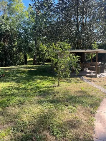 View of grassy yard featuring a patio area, view of wooded area, and a carport