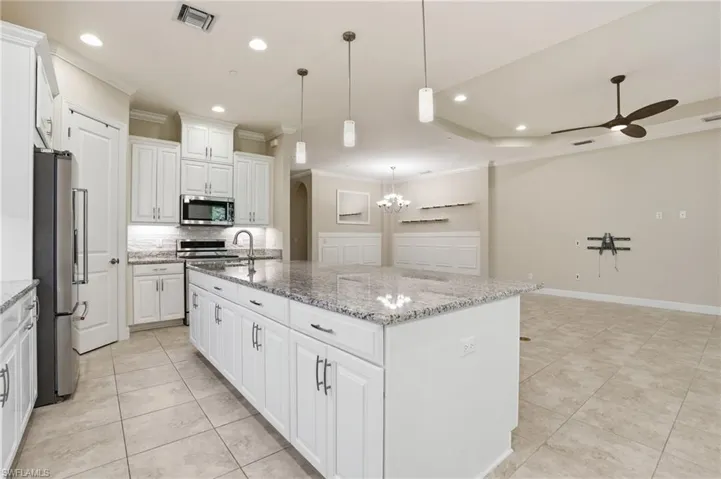 Kitchen featuring white cabinetry, an island with sink, stainless steel appliances, crown molding, and hanging lights