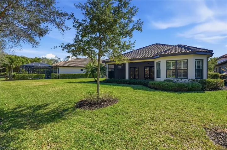 Back of property with a lawn, stucco siding, a tiled roof, and a sunroom