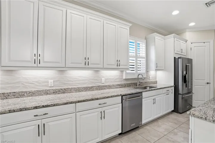 Kitchen with white cabinetry, crown molding, light stone countertops, stainless steel appliances, and decorative backsplash