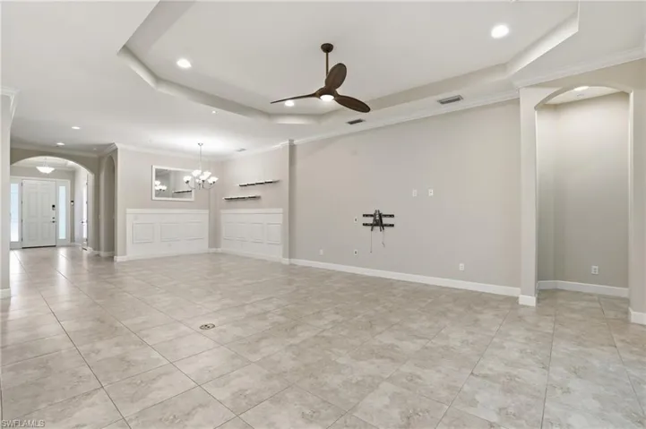 Spare room featuring arched walkways, crown molding, a raised ceiling, ceiling fan, and a chandelier