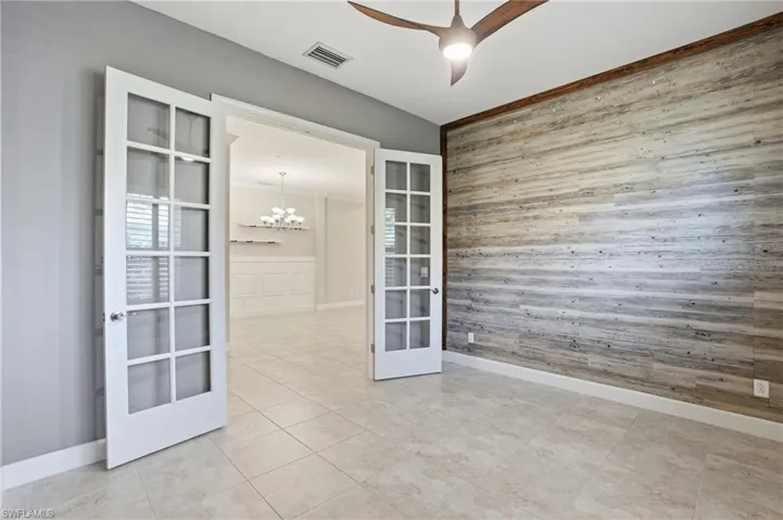 Empty room with wood walls, suspended lighting, french doors, an accent wall, and a ceiling fan