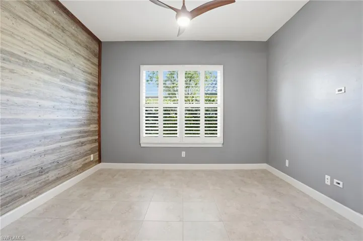 Spare room with wooden walls, an accent wall, ceiling fan, and light tile patterned floors