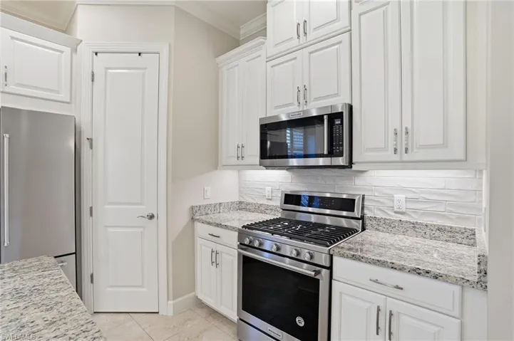Kitchen featuring stainless steel appliances, white cabinets, light stone counters, crown molding, and light tile patterned flooring
