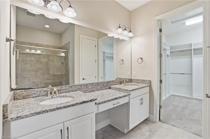 Bathroom with a spacious closet, double vanity, a shower stall, and light colored carpet