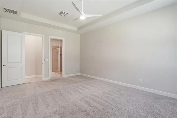 Unfurnished bedroom featuring a tray ceiling, light carpet, a ceiling fan, and connected bathroom