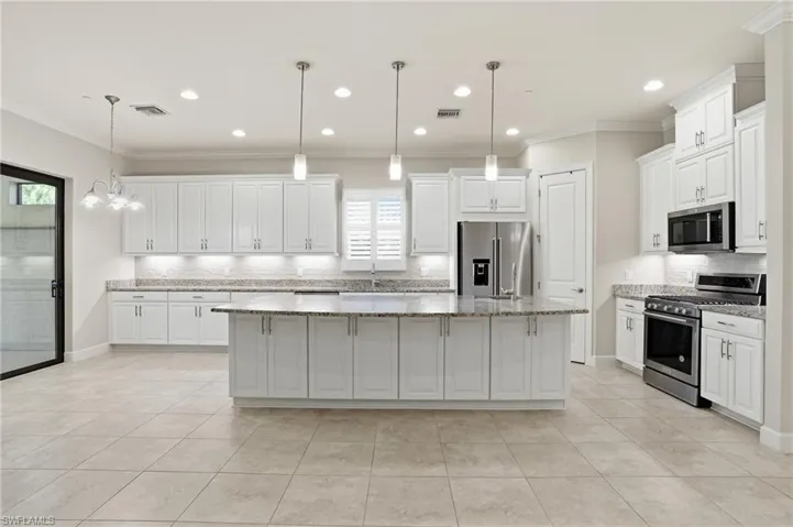 Kitchen with decorative backsplash, stainless steel appliances, a center island, white cabinetry, and light stone countertops