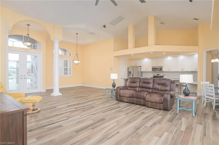 Living room featuring high vaulted ceiling, light wood-type flooring, decorative columns, and french doors
