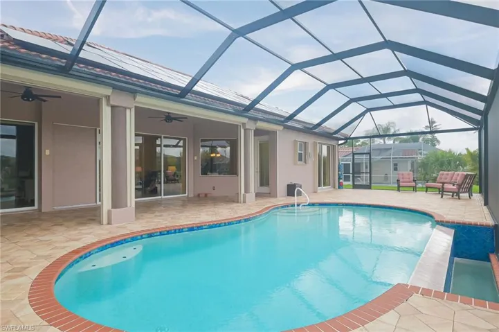 View of pool with glass enclosure, a patio area, and ceiling fan