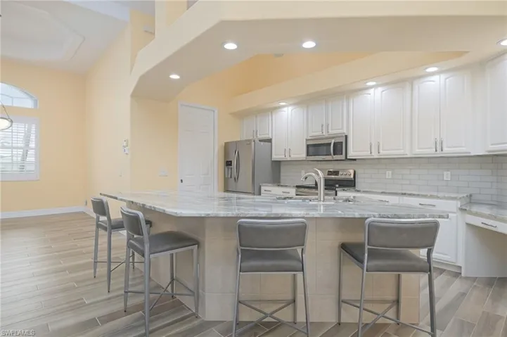 Kitchen with light hardwood / wood-style floors, appliances with stainless steel finishes, white cabinets, light stone counters, and vaulted ceiling