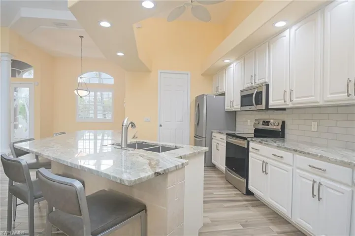 Kitchen with white cabinetry, light hardwood / wood-style floors, a center island with sink, appliances with stainless steel finishes, and backsplash