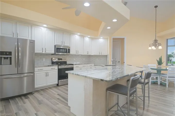 Kitchen with light hardwood / wood-style flooring, decorative light fixtures, backsplash, white cabinets, and appliances with stainless steel finishes
