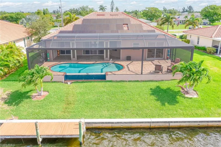 View of pool with a yard, glass enclosure, a water view, and a patio