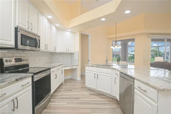Kitchen with decorative light fixtures, backsplash, sink, white cabinets, and appliances with stainless steel finishes