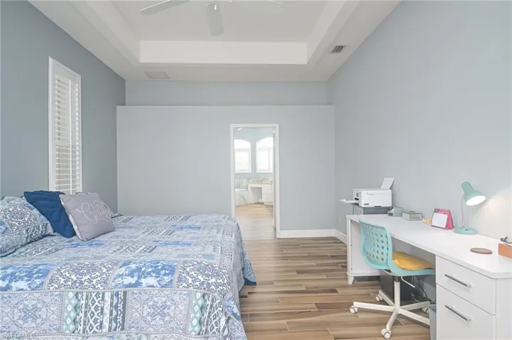 Bedroom featuring ceiling fan, connected bathroom, light hardwood / wood-style flooring, and a tray ceiling