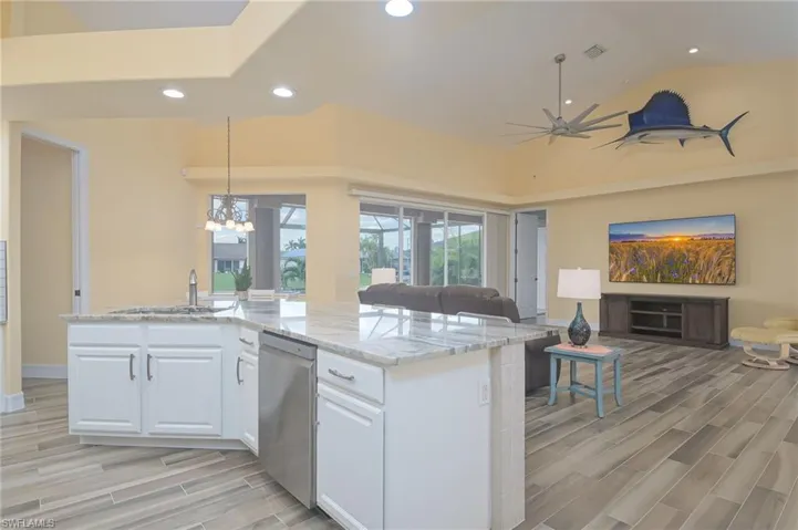 Kitchen with light stone countertops, stainless steel dishwasher, white cabinets, pendant lighting, and sink