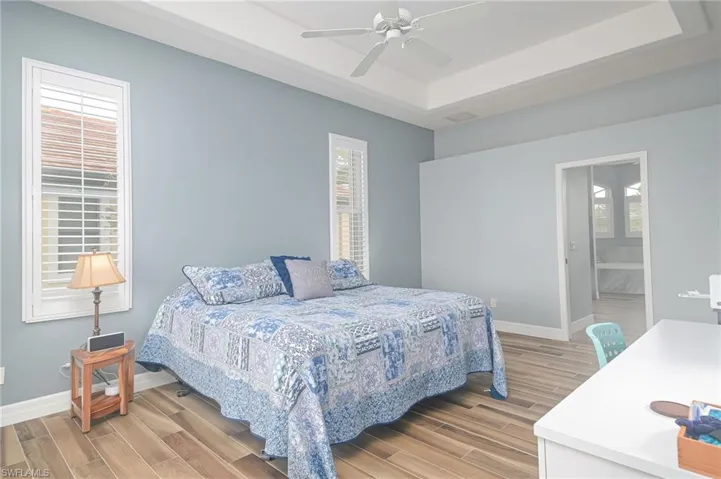 Bedroom with ceiling fan, multiple windows, light wood-type flooring, and ensuite bathroom